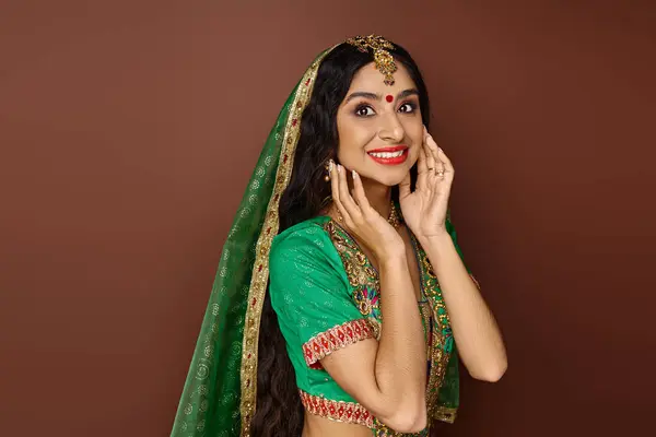 Hermosa mujer india en traje tradicional con bindi y velo verde sonriendo felizmente a la cámara - foto de stock