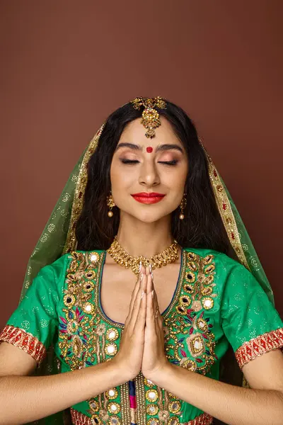 Vertical shot of beautiful indian woman in national clothes showing praying gesture with closed eyes — Stock Photo