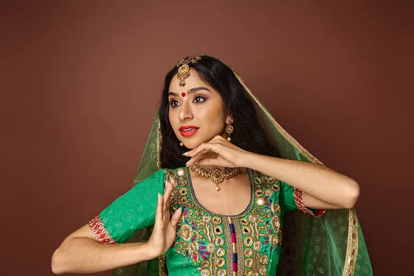 Belle jeune femme indienne en costume traditionnel avec des accessoires gesticulant et détournant les yeux — Photo de stock