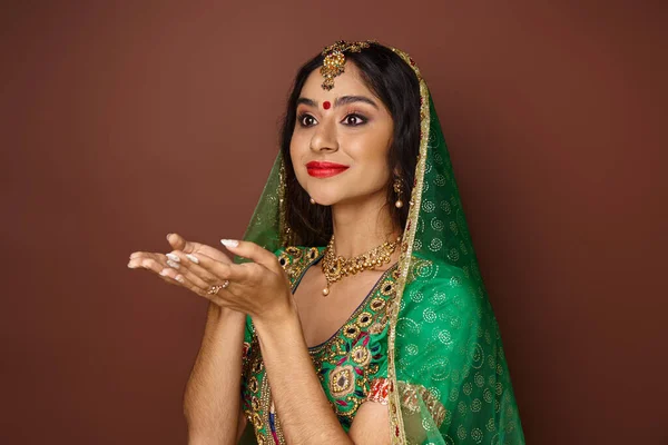 Belle jeune femme indienne en vêtements traditionnels posant avec les paumes ouvertes et regardant loin — Photo de stock
