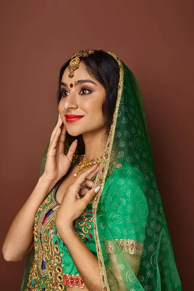 Вертикальний знімок веселки індійської жінки в традиційному одязі з аксесуарами рукою на щоці — стокове фото