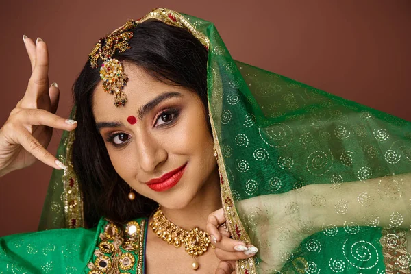 Atractiva mujer india alegre con punto bindi y velo verde gestos y mirando a la cámara - foto de stock