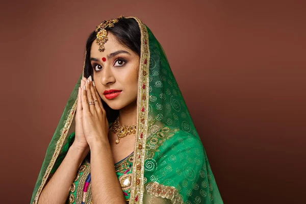 Jolie femme indienne en costume traditionnel avec point bindi montrant geste de prière et détournant les yeux — Photo de stock