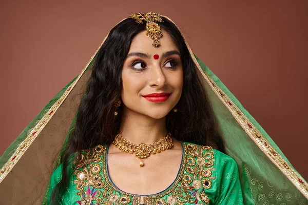 Веселая молодая индийская женщина с точкой бинди на лбу и зеленой вуалью, позирующая и отворачивающаяся — стоковое фото
