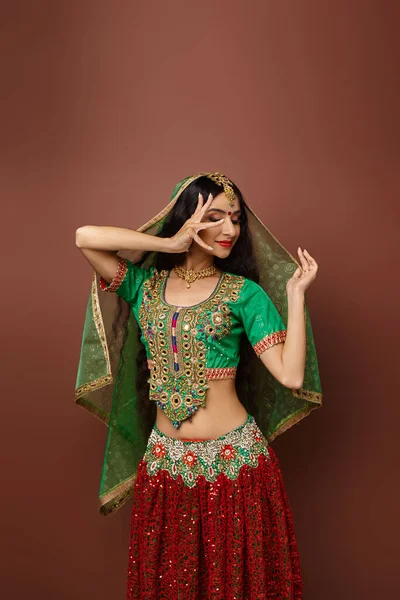 Tiro vertical de mujer india en choli verde con gesto de punto bindi mientras baila y mira hacia otro lado - foto de stock