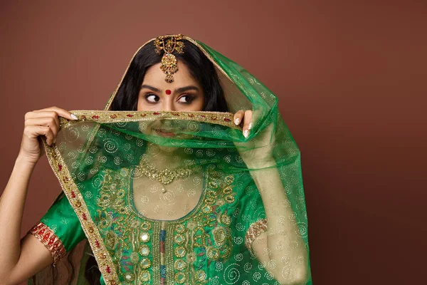 Atraente jovem indiana mulher com bindi ponto na testa cobrindo rosto com seu véu verde — Fotografia de Stock