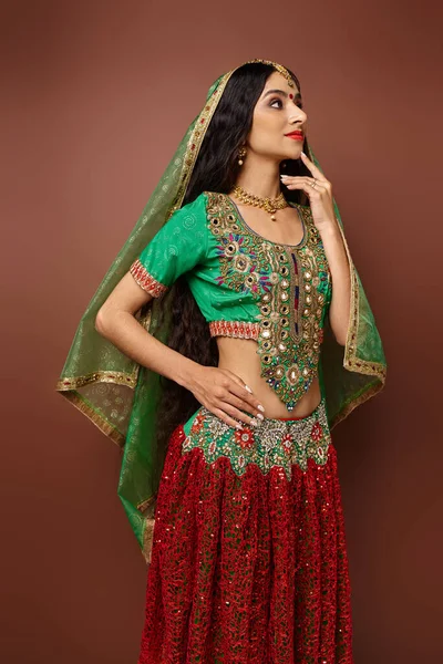 Вертикальный снимок красивой индийской женщины в национальной одежде с зеленой вуалью, позирующей рукой на бедре — стоковое фото
