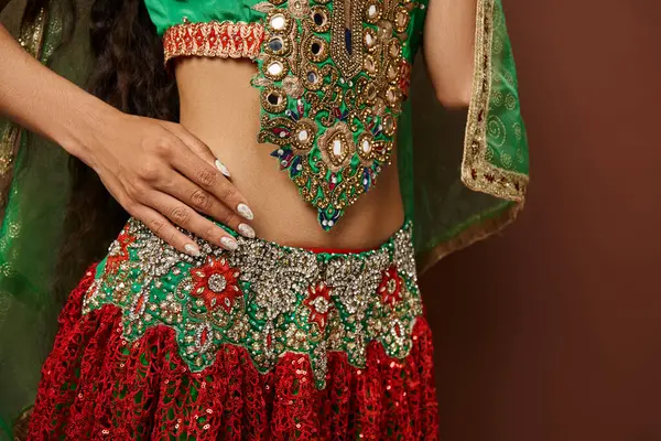 Vue recadrée du ventre de la jeune femme indienne en costume national avec accessoires sur fond marron — Photo de stock