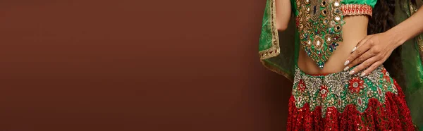 Vue recadrée du ventre de la jeune femme indienne en costume traditionnel sur fond brun, bannière — Photo de stock