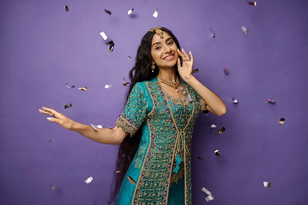 Joyful indian woman with accessories in blue sari smiling at camera posing under confetti rain — Stock Photo