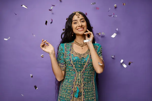 Jovem mulher indiana alegre com cabelos longos sorrindo para a câmera enquanto posando sob chuva confete — Fotografia de Stock