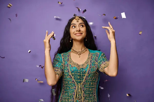 Attractive jolly indian woman in national costume posing under confetti rain on purple backdrop — Stock Photo