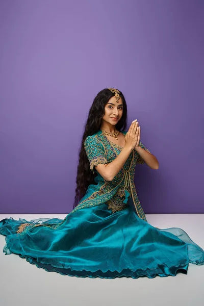 Vertical shot of young indian woman in blue sari sitting on floor and showing praying gesture — Stock Photo