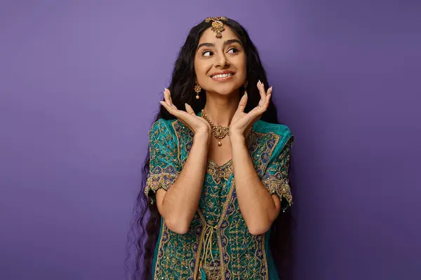 Heureuse femme indienne avec les cheveux longs en sari bleu posant sur fond violet avec les mains près du visage — Photo de stock