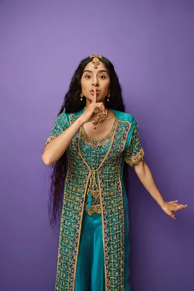 Atractiva mujer india en sari tradicional azul posando sobre fondo púrpura mostrando gesto de silencio - foto de stock