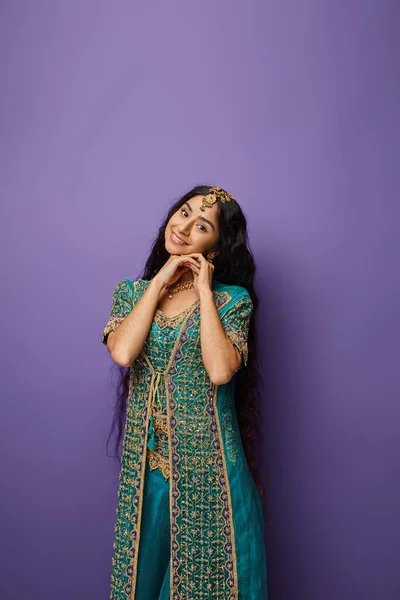 Jovem mulher indiana atraente em traje nacional posando em pano de fundo roxo e sorrindo para a câmera — Fotografia de Stock