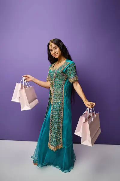 Plan vertical de jeune femme indienne joyeuse en costume traditionnel posant avec des sacs à provisions dans les mains — Photo de stock