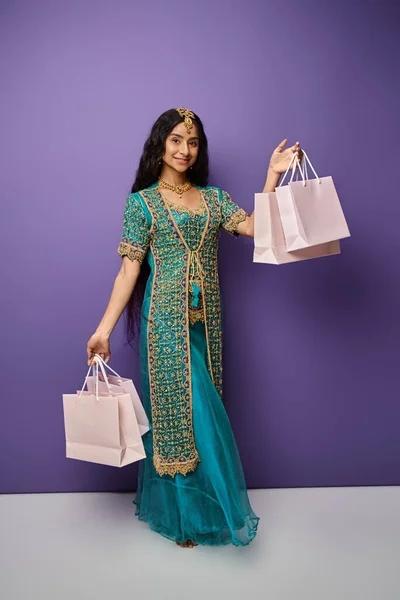 Tiro vertical de mulher índia sorridente em roupas tradicionais com sacos de compras sorrindo para a câmera — Fotografia de Stock