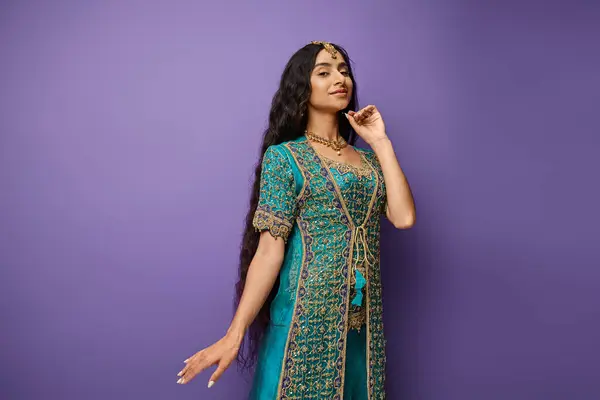 Ziemlich fröhliche indische Frau in blauen traditionellen Sari posiert auf lila Hintergrund mit der Hand in der Nähe Gesicht — Stockfoto