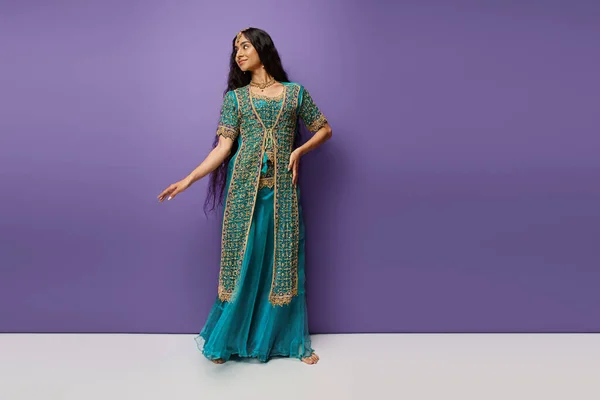 Belle jeune femme indienne aux cheveux longs en sari bleu avec accessoires sur fond violet — Photo de stock