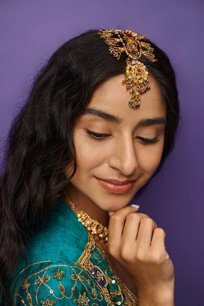 Bonita jovem indiana mulher em sari azul com acessórios posando com a mão no queixo e olhando para baixo — Fotografia de Stock