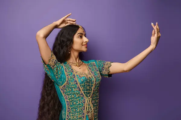 Atractiva mujer india joven en traje nacional gesto mientras baila sobre fondo púrpura - foto de stock