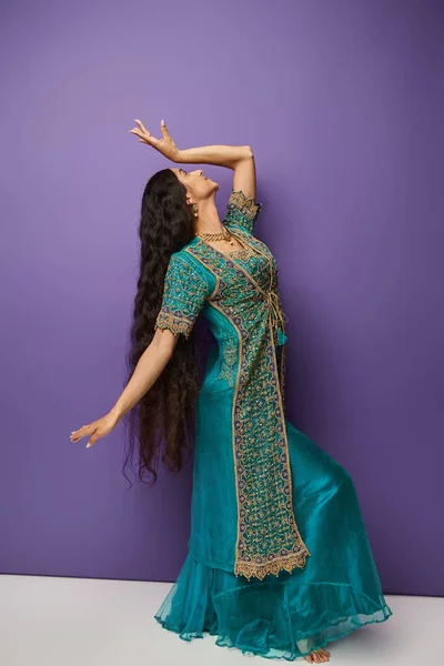 Junge Indianerin in blauem Sari mit Accessoires gestikuliert, während sie auf violettem Hintergrund tanzt — Stockfoto