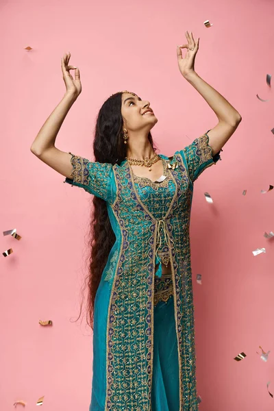Vertical shot of attractive indian woman in blue sari gesturing while dancing under confetti rain — Stock Photo
