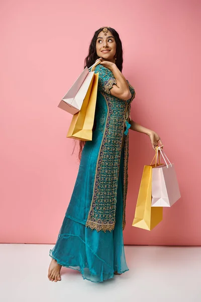 Belle femme indienne posant de profil avec des sacs à provisions tournant la tête et souriant joyeusement — Photo de stock