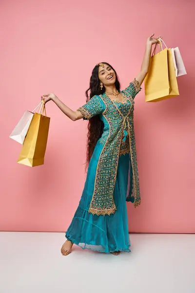 Attraente giovane donna indiana in costume nazionale in posa con borse della spesa e sorridente alla macchina fotografica — Foto stock