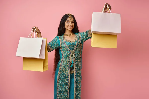 Fröhliche indische Frau in traditionellem blauen Sari posiert mit Einkaufstüten in den Händen und lächelt in die Kamera — Stockfoto
