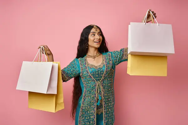 Mulher indiana feliz em traje nacional com acessórios segurando sacos de compras em pano de fundo rosa — Fotografia de Stock