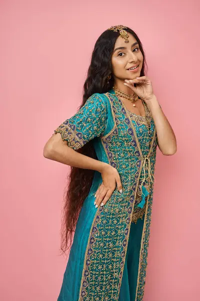 Tiro vertical de mujer india alegre en traje nacional con la mano cerca de la barbilla sonriendo a la cámara - foto de stock