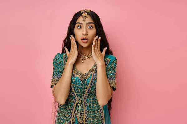 Choqué jeune femme indienne en costume traditionnel posant avec les mains près du visage avec la bouche ouverte — Photo de stock