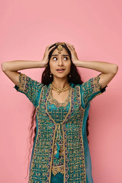 Tiro vertical de joven mujer india sorprendida en traje nacional posando con las manos en la cabeza - foto de stock