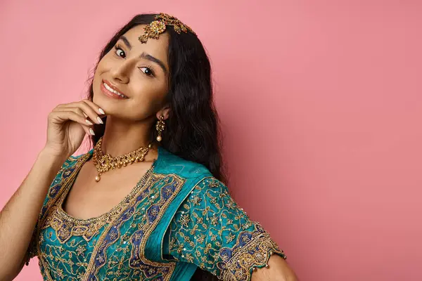 Modèle féminin indien joyeux avec accessoires en sari bleu posant sur fond rose avec la main près du visage — Photo de stock