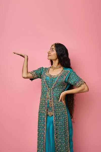 Tiro vertical de bela jovem mulher indiana em traje nacional posando com a palma aberta olhando para longe — Fotografia de Stock
