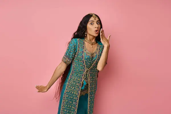 Surprised beautiful indian woman in national costume posing on pink backdrop with hand near mouth — Stock Photo