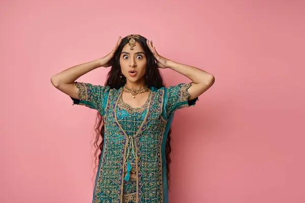 Surprised young indian woman in traditional costume with hands on head posing on pink backdrop — Stock Photo