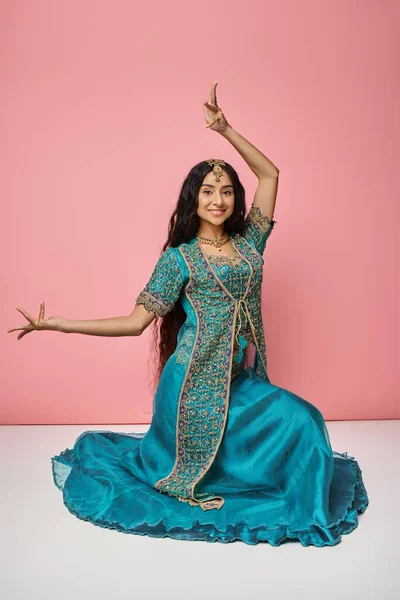 Jolly indian woman in traditional blue sari sitting on floor and gesturing actively on pink backdrop — Stock Photo