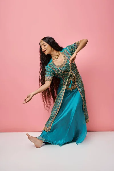 Mujer india guapa en sari azul tradicional haciendo gestos mientras baila sobre fondo rosa - foto de stock