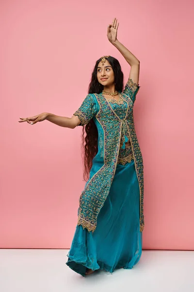 Attrayant jeune femme indienne en vêtements nationaux gestuelle tout en dansant sur fond rose — Photo de stock