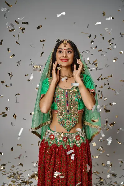 Tiro vertical de joven hermosa mujer india en traje nacional con bindi punto bajo la lluvia confeti - foto de stock
