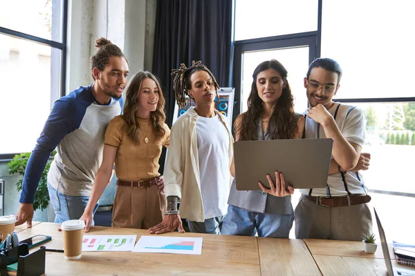 Lächelndes und inspiriertes multikulturelles Team beim Blick auf den Laptop während der Arbeit am Start-up im modernen Büro — Stockfoto