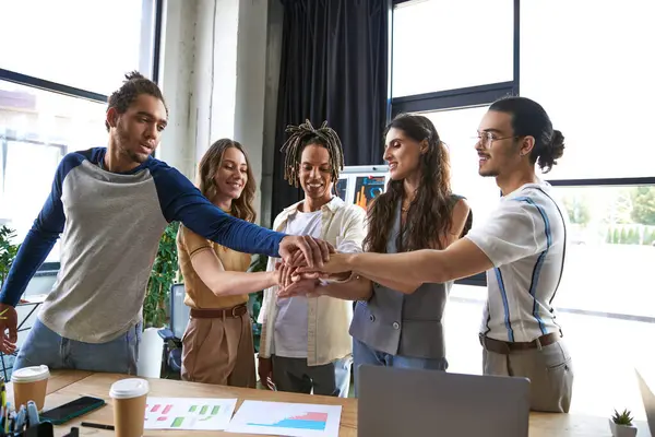 Pessoas de negócios multiétnicos felizes juntando as mãos perto de gráficos e laptop no escritório, sinal de unidade — Fotografia de Stock