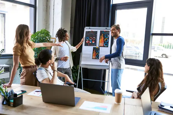Creative multiethnic team talking and sharing ideas near flip chart with  infographics in office — Stock Photo