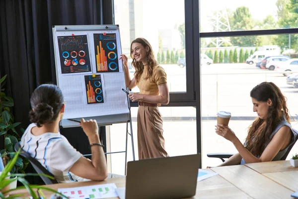 Smiling businesswoman near flip chart with infographics during teamwork on startup in office — Stock Photo