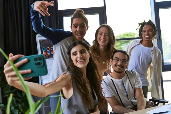 Happy woman taking photo on smartphone with excited multicultural team in coworking office — Stock Photo