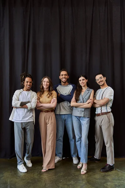 Squadra multiculturale sorridente in elegante abbigliamento casual con braccia incrociate vicino drappeggio nero in ufficio — Foto stock