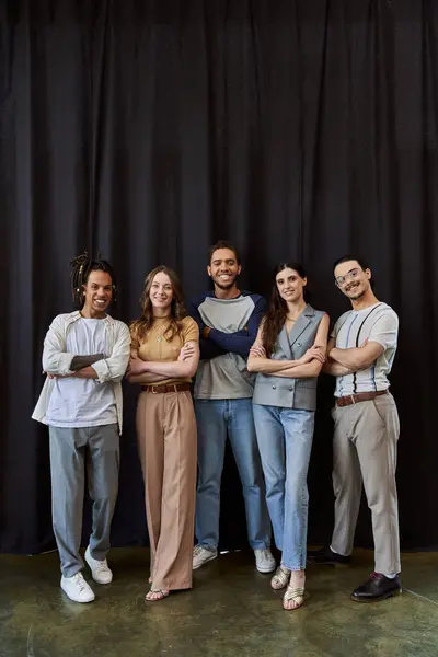 Smiling multicultural team in stylish casual attire with folded arms near black drape in office — Stock Photo